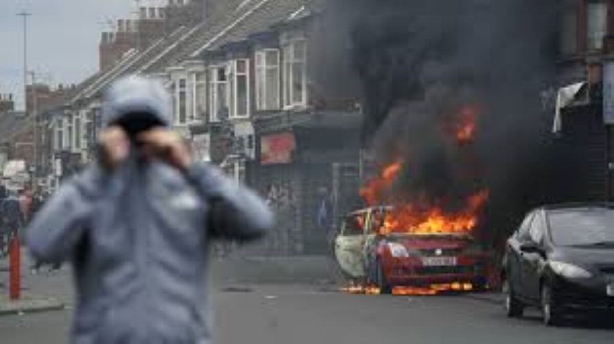 "Street in chaos as a car burns during UK riots."