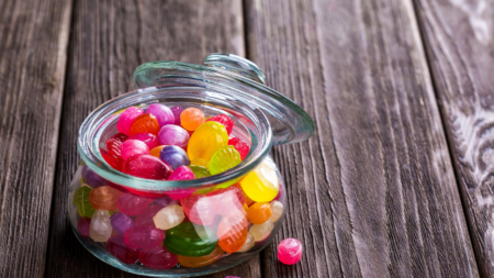 Jar filled with colorful hard candies on a wooden table.