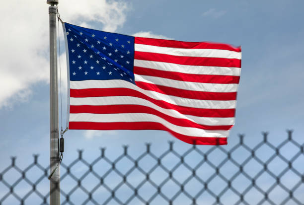 US flag flying in the wind, protected by a border protection fence