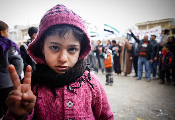 A child showing victory sign, behind him their is crowd protesting.