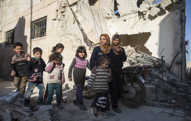 women with many children in front of bombarded buildings in Syria